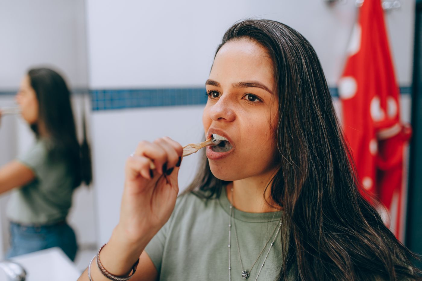 A woman brushing her teeth with a plain wooden-handled brush