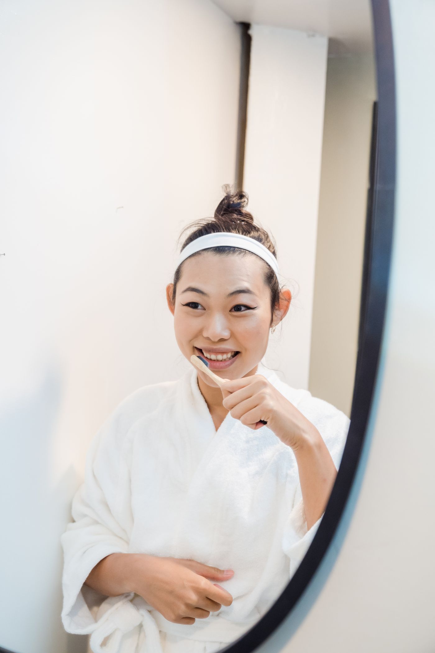 A woman brushing her teeth in front of a bathroom mirror