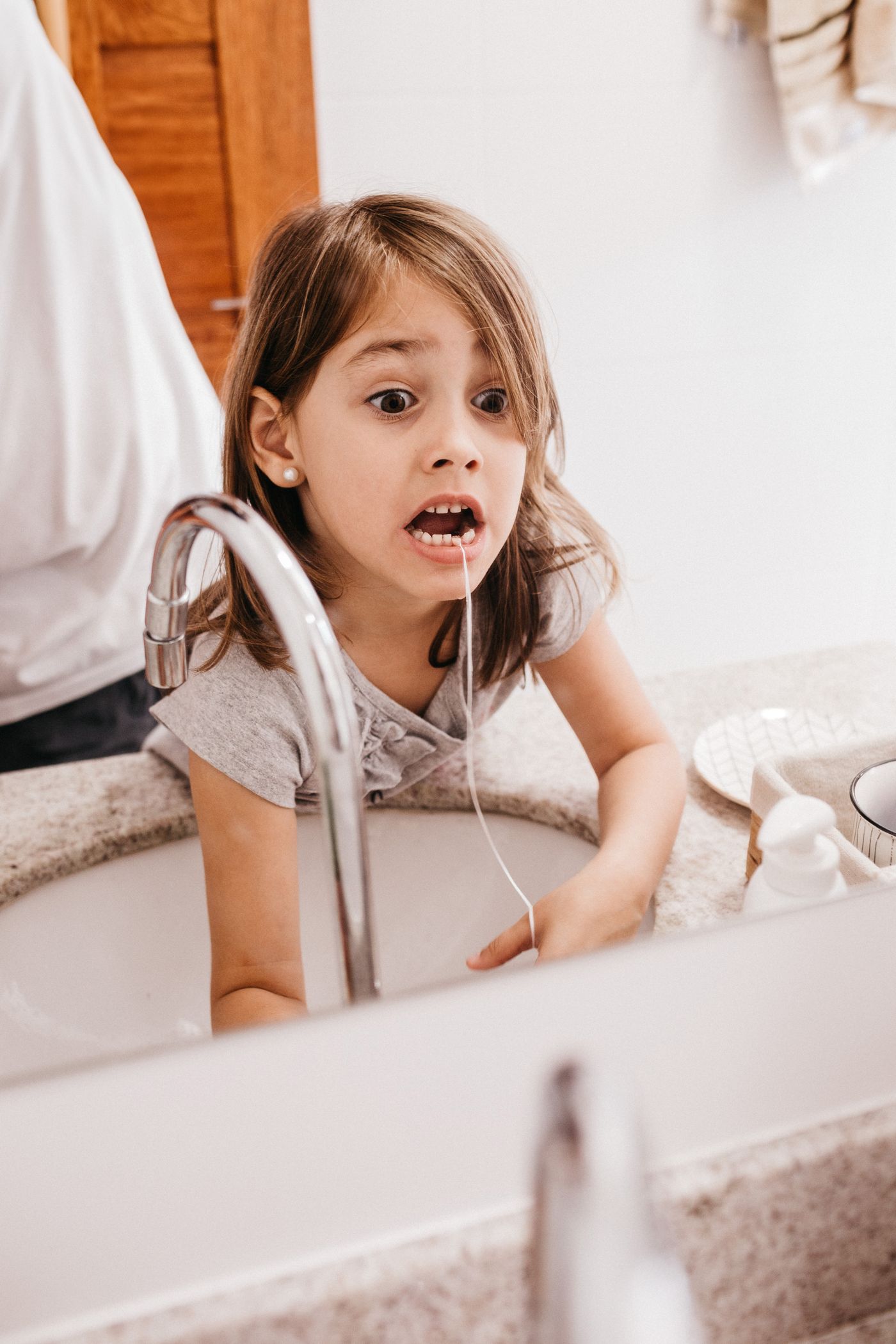 A young girl learning to clean between her teeth at the sink