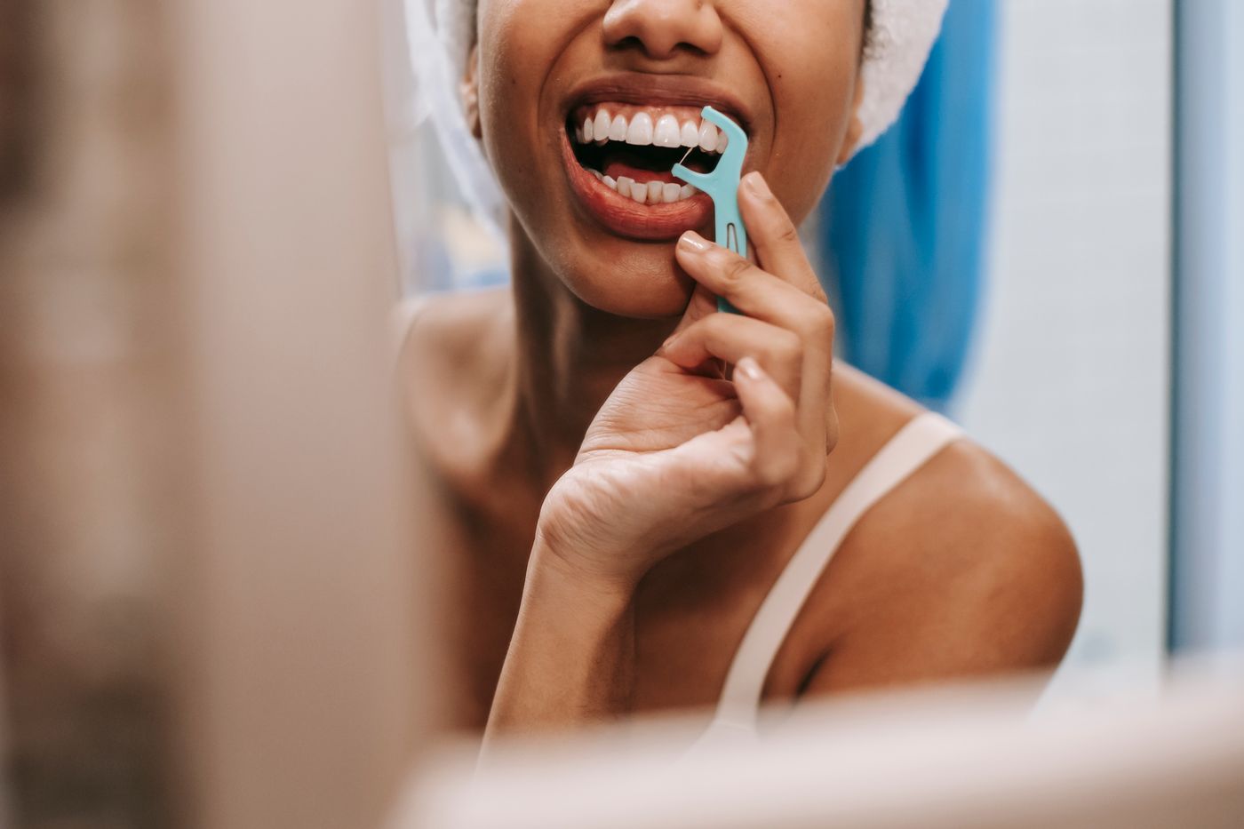 A woman cleaning between her teeth, reflected in a mirror