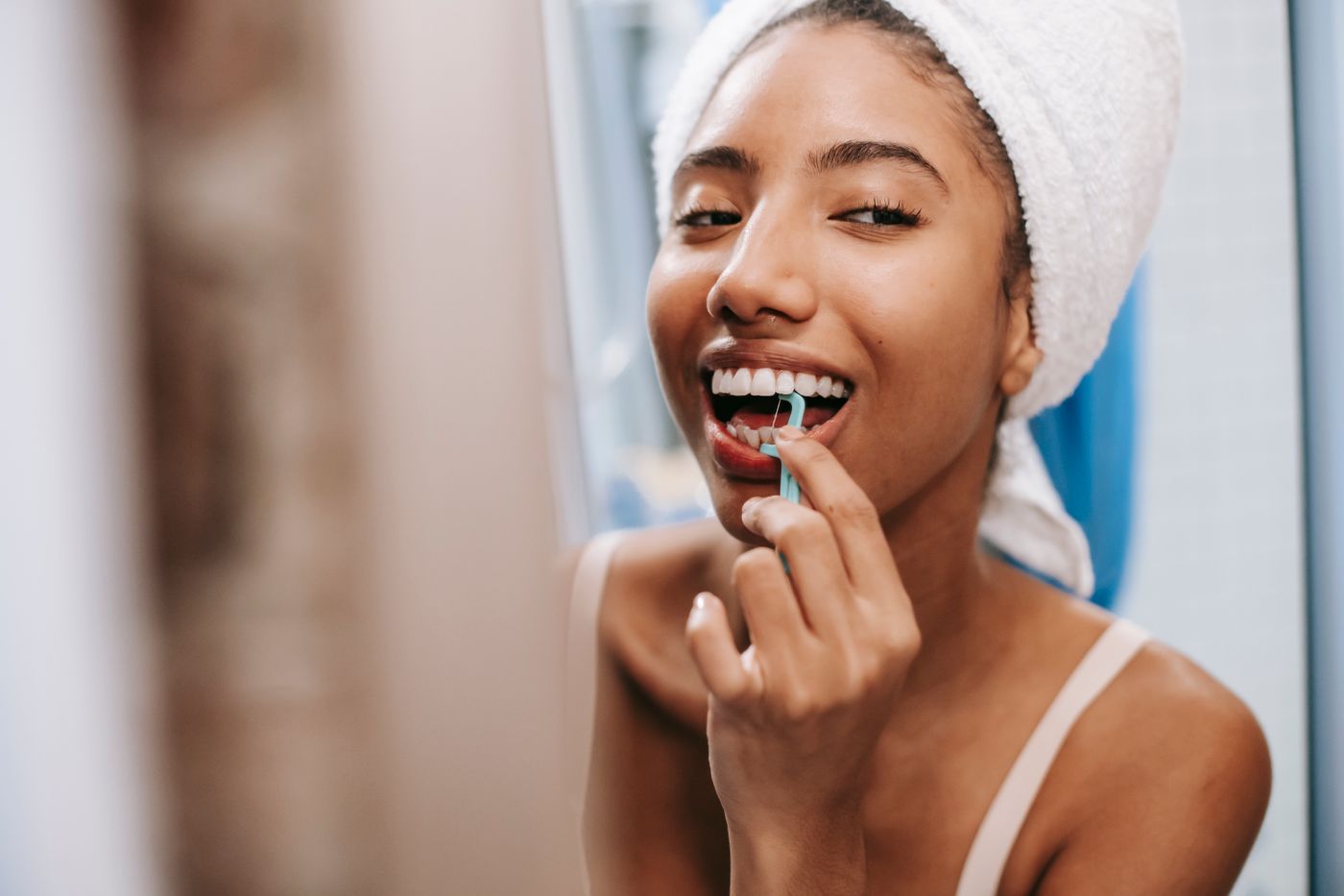 A smiling woman with a towel on her head cleaning between her teeth
