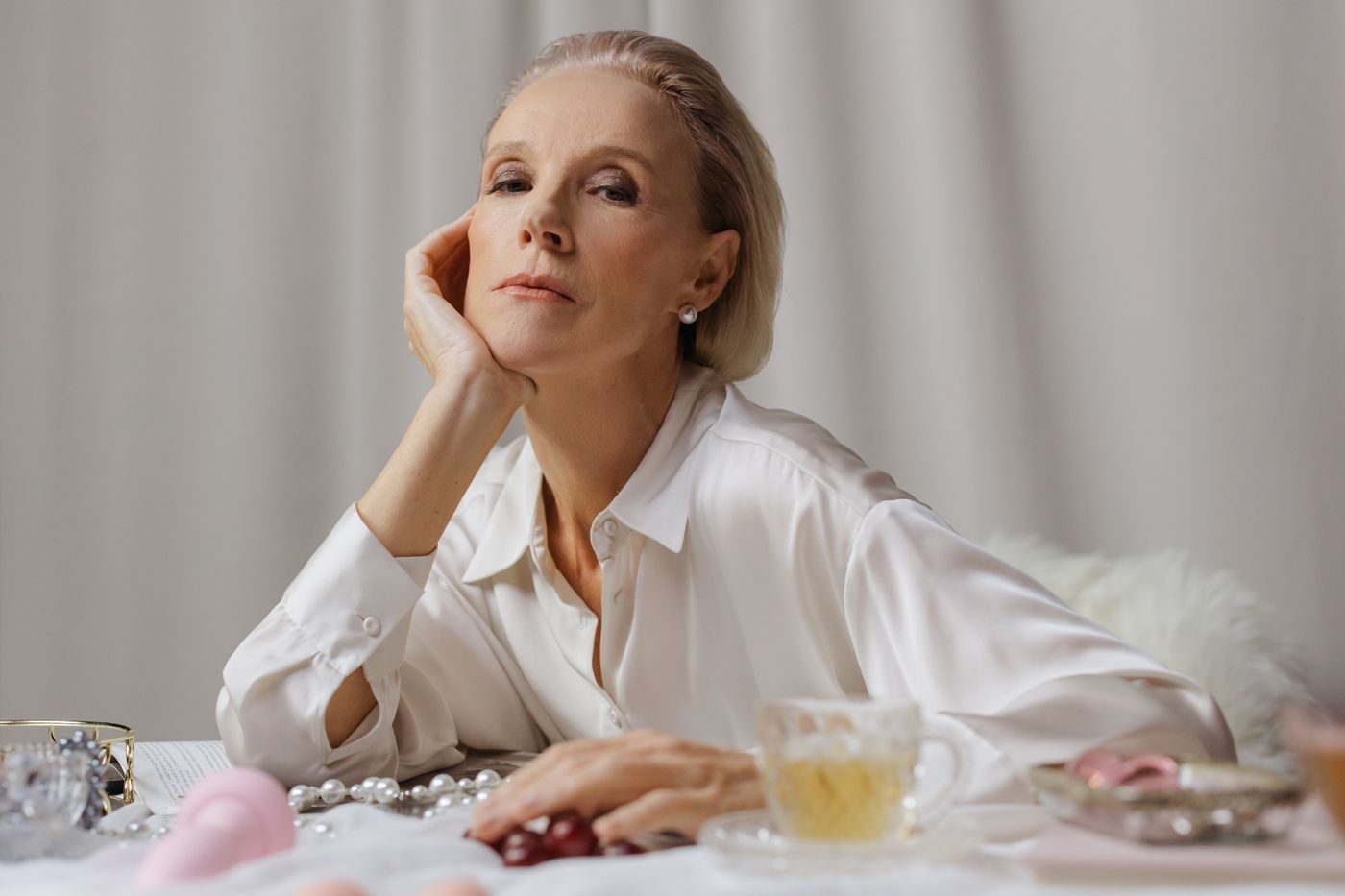 An older woman in a white shirt sitting with a warm drink