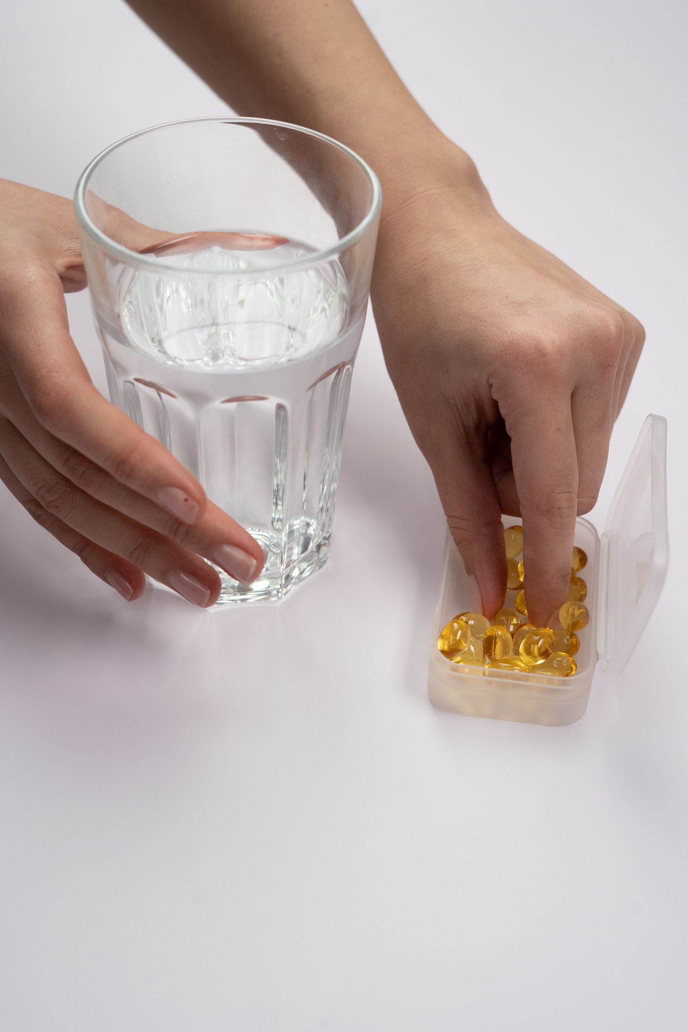 A hand taking a supplement beside a glass of water