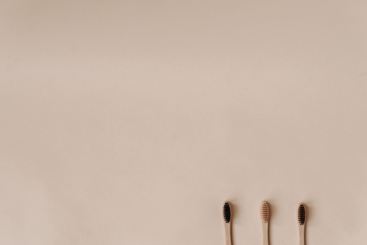 Three bamboo toothbrushes on a plain beige background