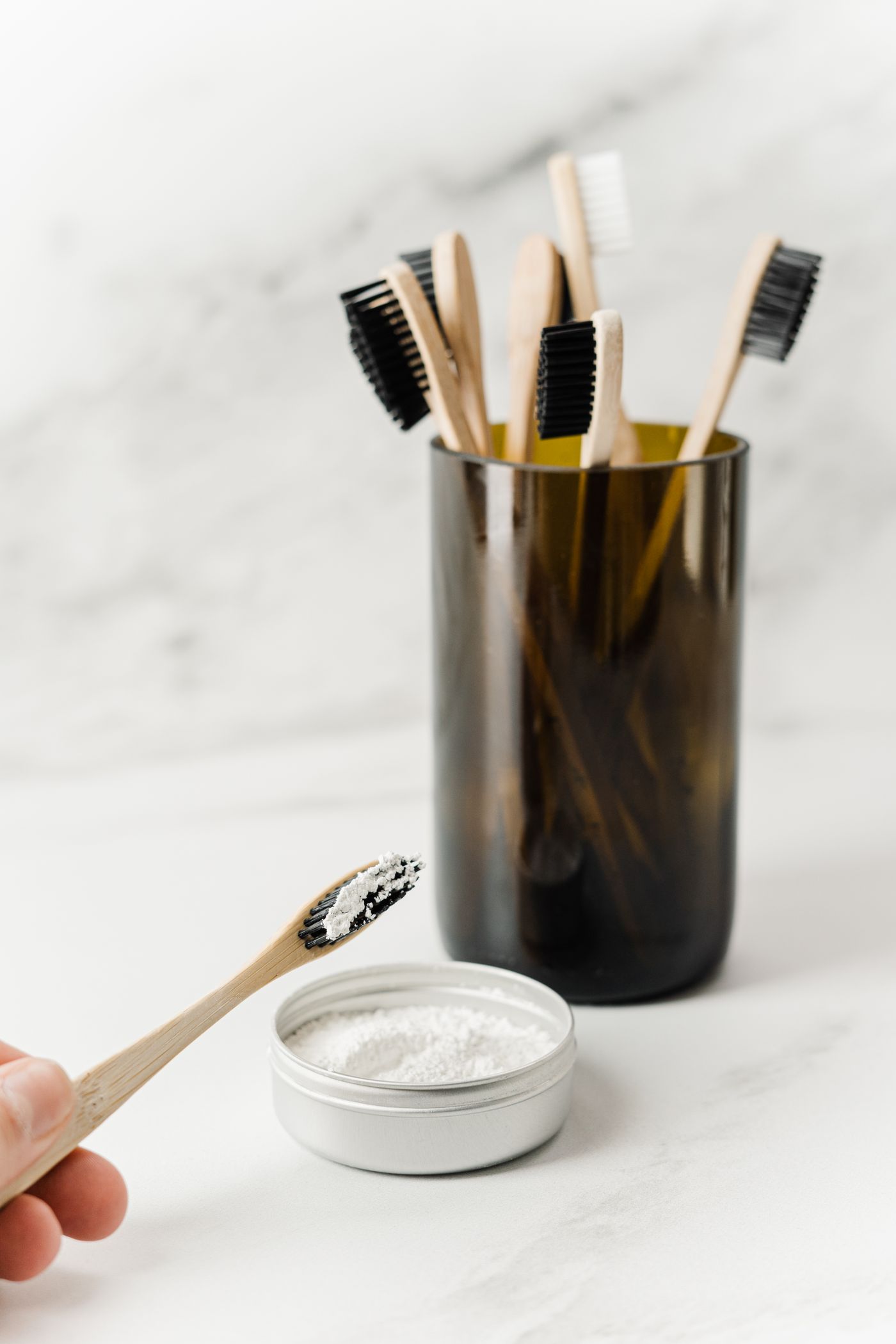 Wooden toothbrushes in a dark tumbler beside a jar of tooth powder