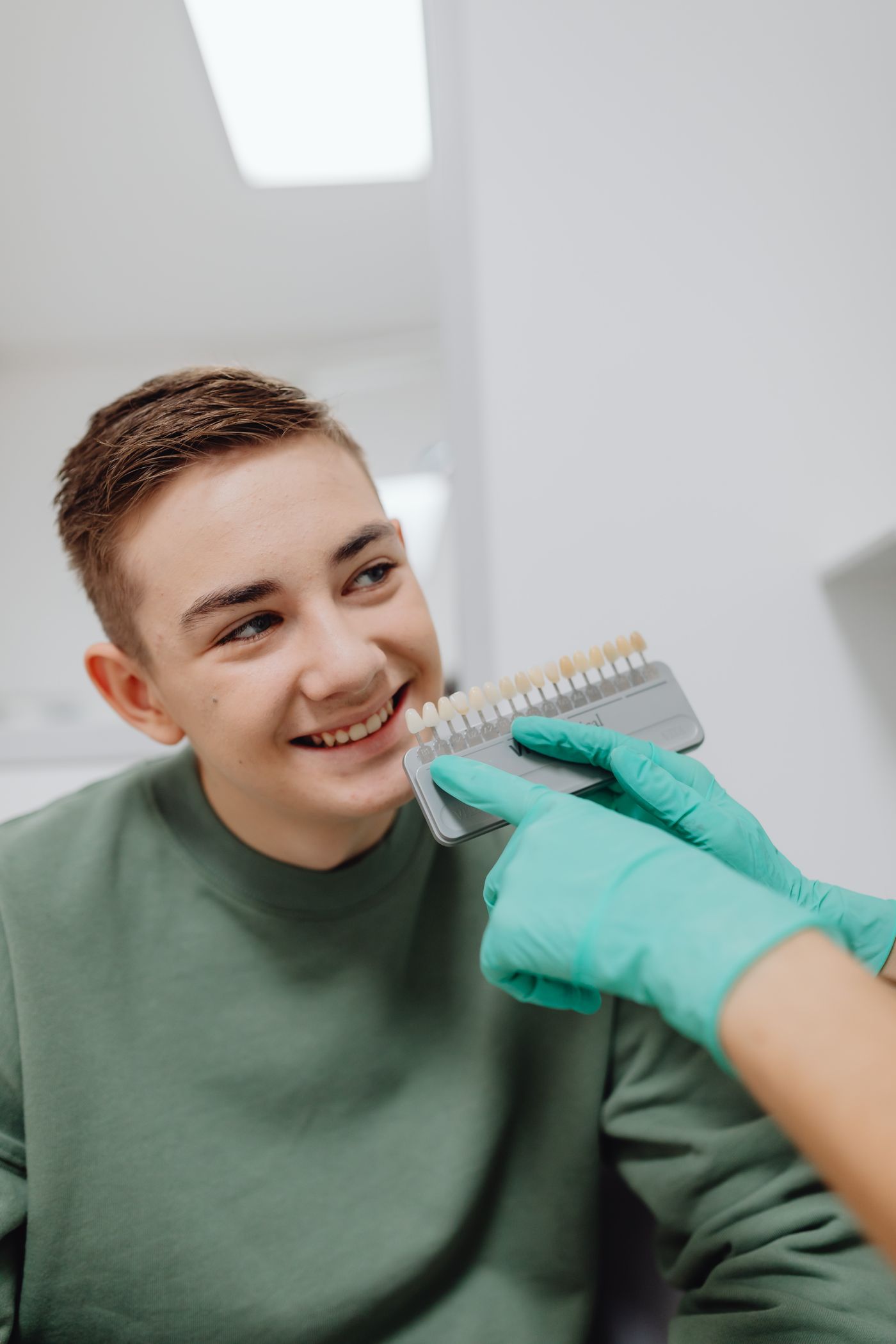 A smiling patient having their tooth shade checked at a dental visit